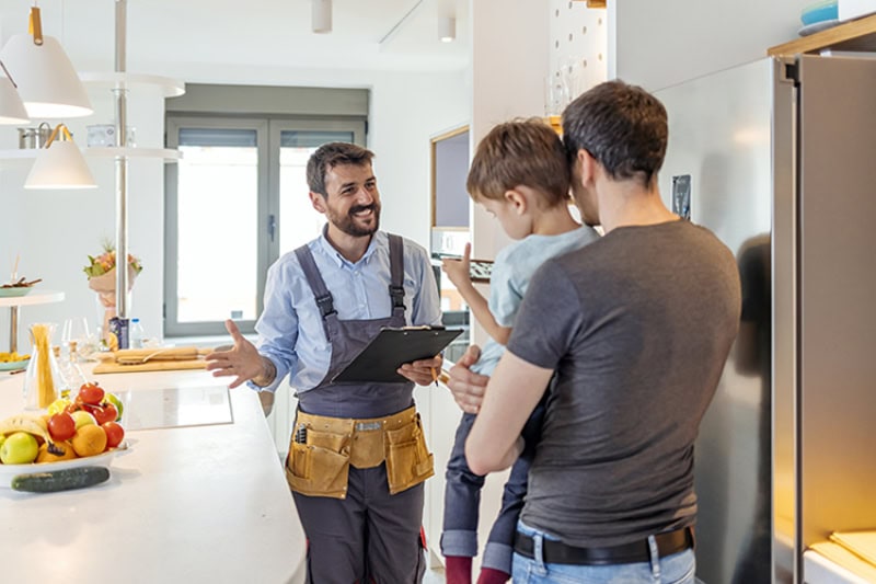 DIY AC Maintenance Checklist. Professional plumber in uniform talking to male client and his small son indoors.