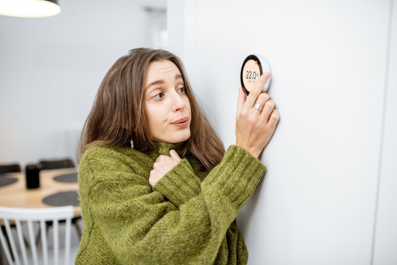 Why Is My Heat Pump Turning On and Off Frequently? A woman turning up the temperature on a thermostat.